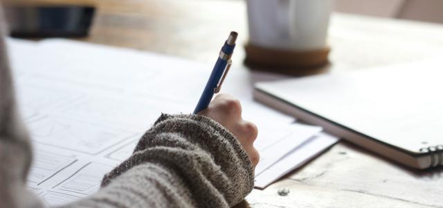 person writing on brown wooden table near white ceramic mug by Unseen Studio courtesy of Unsplash.